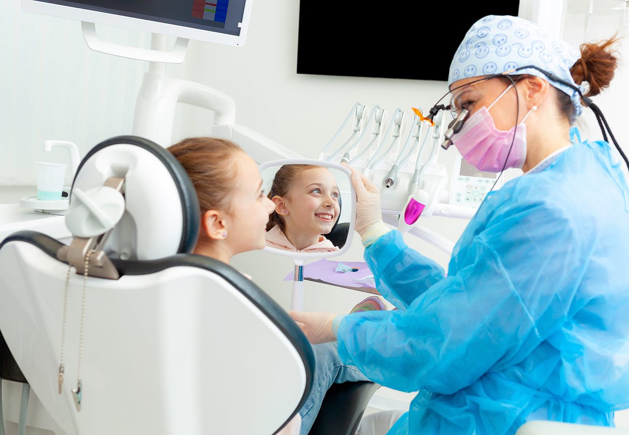 Children's dentistry: Young girl smiles at her reflection during a dental checkup at the dentist's office.