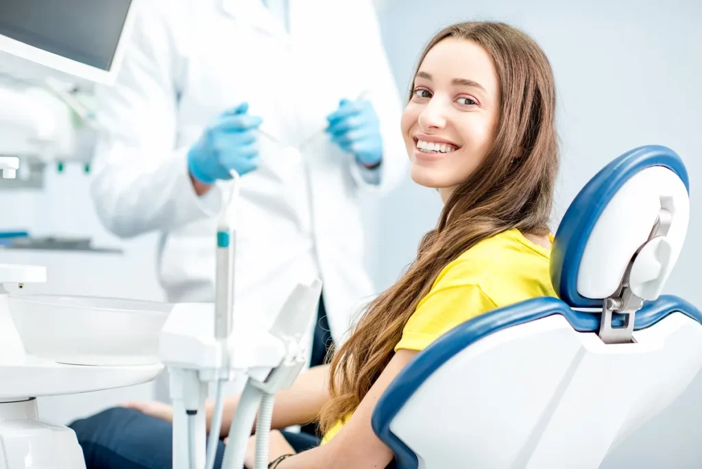 Smiling woman in dental chair for hygiene. Dentist in background. Homepage dental care.